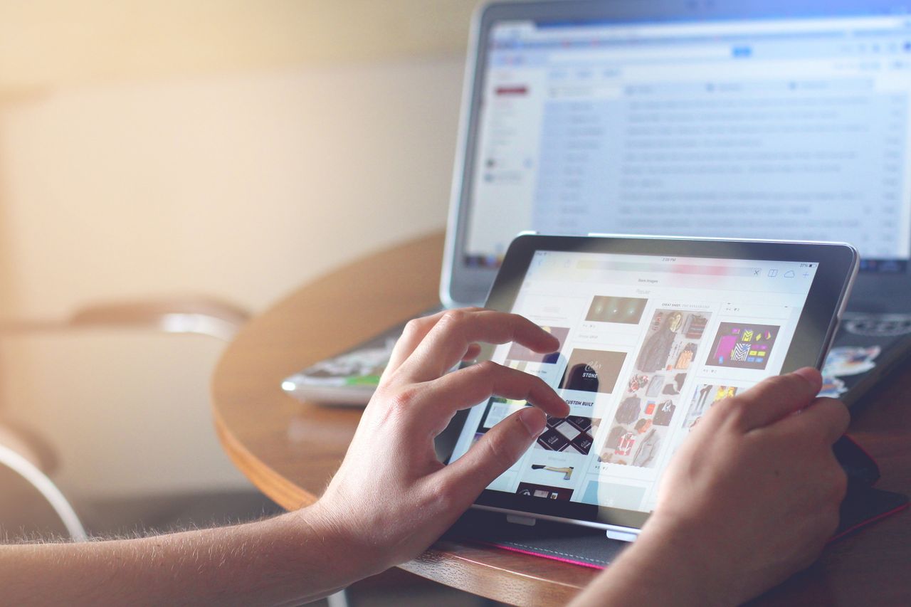 home-img Hands holding a tablet next to a laptop in a home office environment, highlighting online browsing.